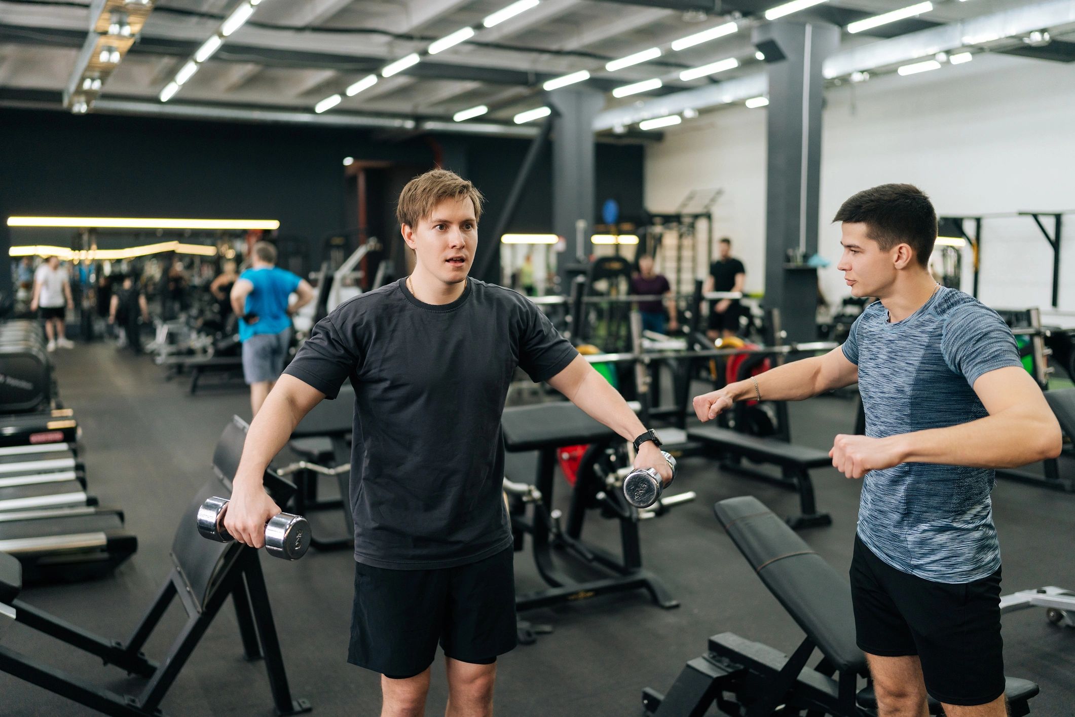 Client performing dumbbell raises with guidance from a trainer