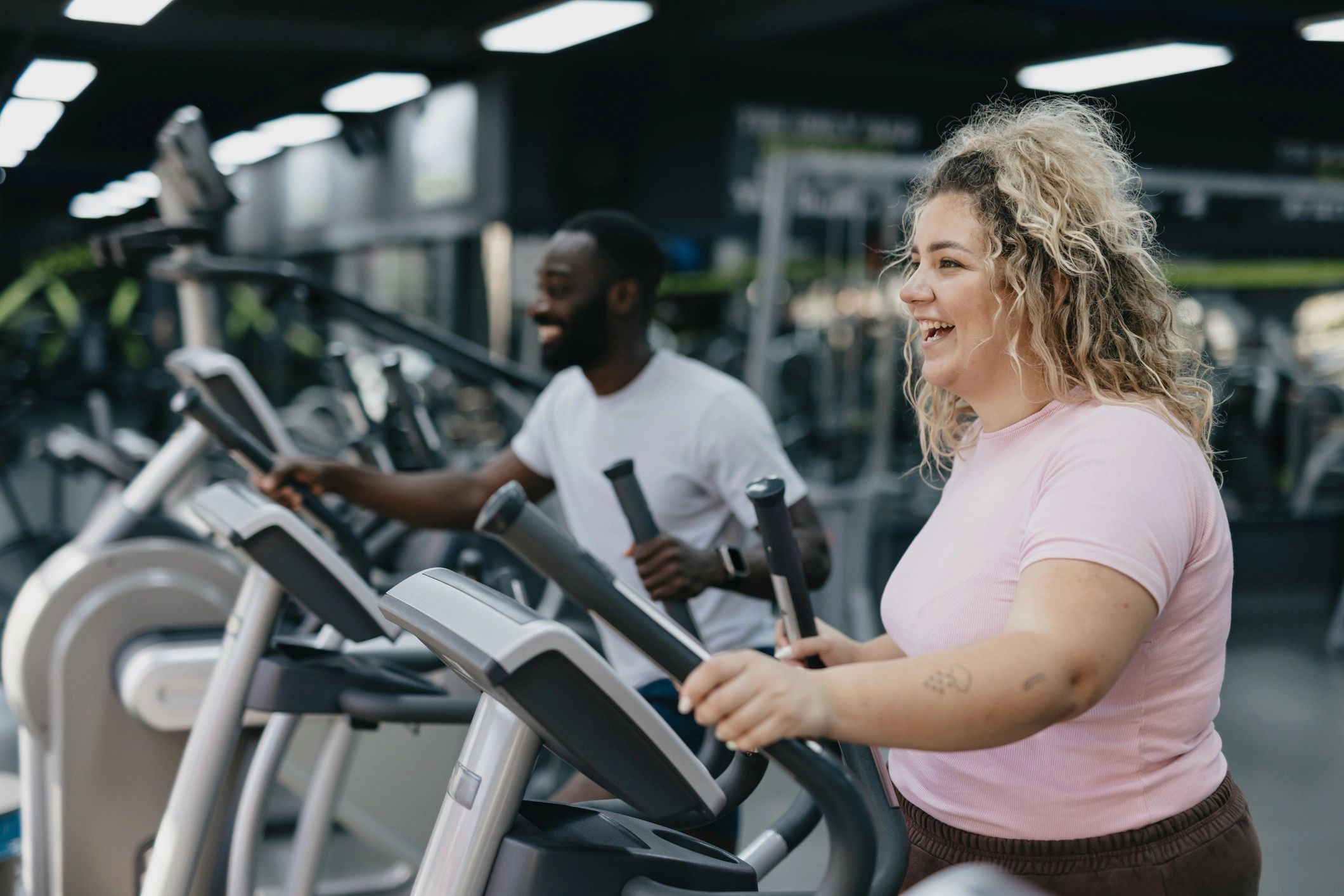Woman and trainer working out on cardio machines in a gym